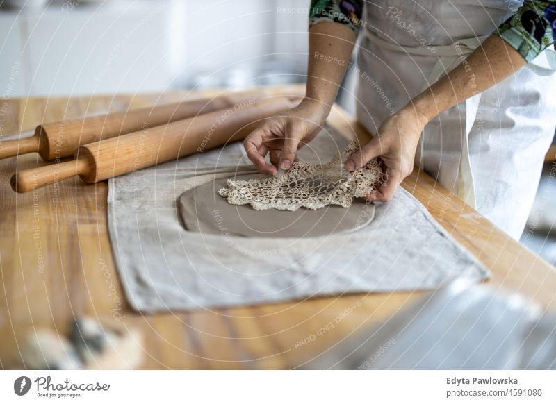 Close-up of craftswoman working on her pottery in workshop hands close up concentration patience traditional molding decorating bowl table wooden clay