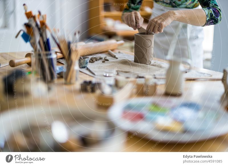 Close-up of craftswoman working on her pottery in workshop hands close up concentration patience traditional molding decorating bowl table wooden clay