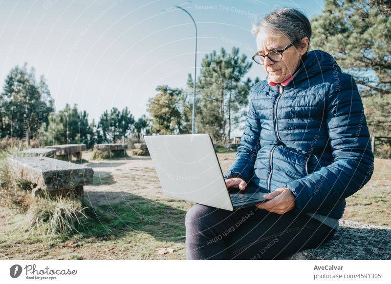 A senior old woman using laptop outdoors internet copy. Starts new habits for the new year. Trekking and healthy life style.Pensioner woman sport. Aging, people, active lifestyle and health concept