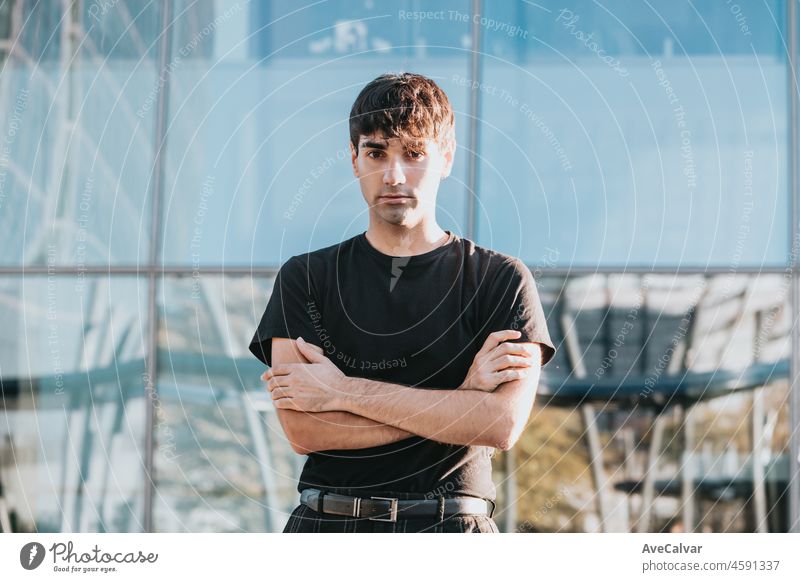 Portrait of cheerful young man in casual with crossed arms serious outdoors in front of a office building in city outdoors. Copy space person businessman