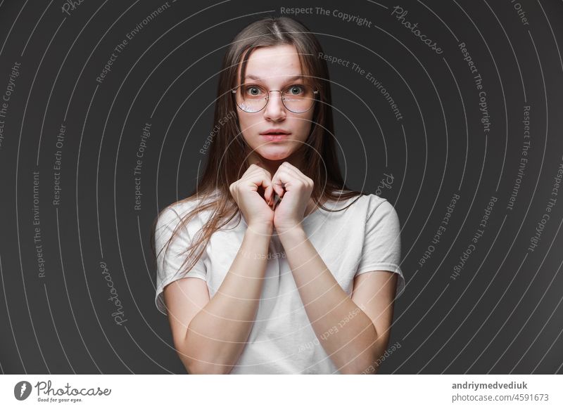 attractive surprised excited scared, terrified teenage girl wear glasses, white t shirt, with brown long hair, isolated on gray background. Concept of human emotions, facial expression, sales, ad.