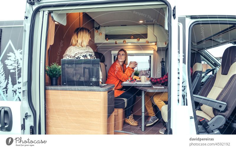 Friends having breakfast in a camper van in the morning friends motorhome women drinking coffee smiling fruit bun table blueberry strawberry caravan interior