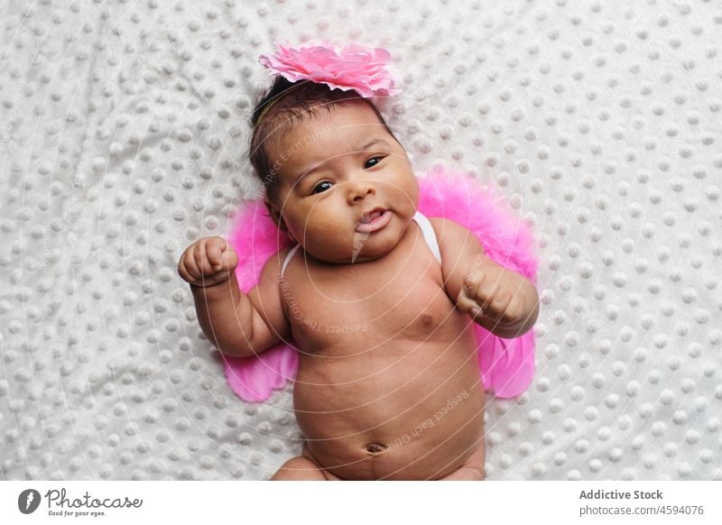 Cute ethnic baby in angel wings and headband girl infant babyhood bare gentle innocent cute childhood little newborn glance adorable lying pure costume