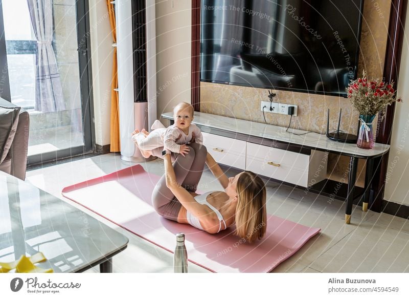 Young mother in sport clothing exercising at home with baby. Online training during coronavirus covid-19 quarantine. Stay fit and safe during pandemic lockdown. Sport, fitness, healthy concept