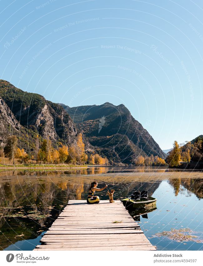 Anonymous female sitting on wooden pier and playing with dog woman traveler water pet boardwalk animal nature road trip owner relax river sun weekend daytime