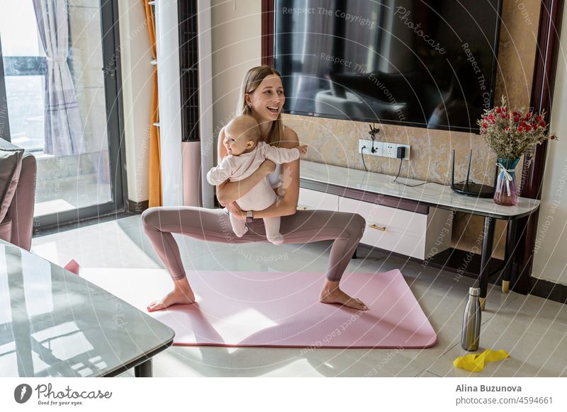 Young mother in sport clothing exercising at home with baby. Online training during coronavirus covid-19 quarantine. Stay fit and safe during pandemic lockdown. Sport, fitness, healthy concept