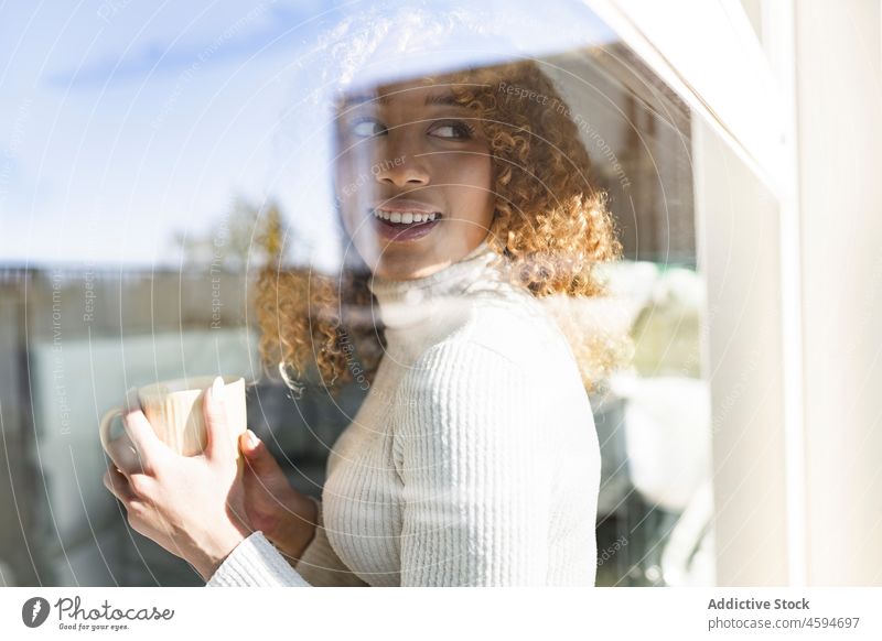 Black woman sitting on windowsill with cup and blanket drink beverage cozy comfort plaid rest relax tea female mug hot drink chill ethnic lady lounge black