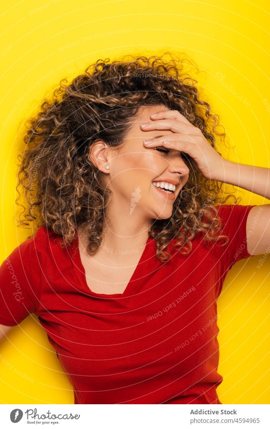 Young woman laughing and covering eyes with hands curly hair bright young colorful style happy cheerful trendy joy casual positive vibrant hand on head smile