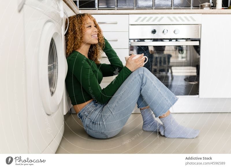 Smiling ethnic woman sitting on sofa with cup of coffee home hot drink comfort relax rest kitchen positive chill smile oven enjoy beverage leisure content cozy