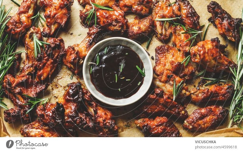 Closeup of roasted chicken wings with baroque sauce and rosemary on baking sheet. Flavorful marinated meat with herbs and spices. Cooking finger-food at home. Top view.