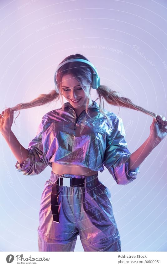 Futuristic female in stylish outfit standing in studio with neon illumination woman illuminate smile listen style futuristic headphones 80s personality happy