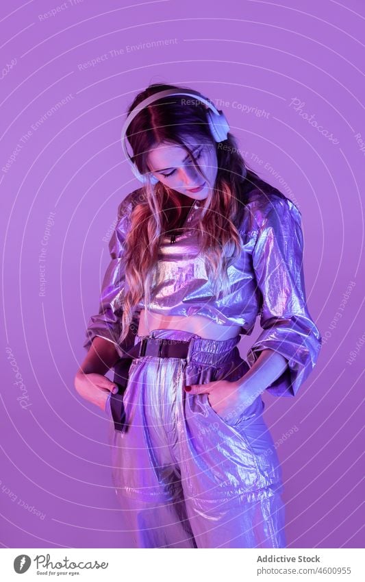 Futuristic female in stylish outfit standing in studio with neon illumination woman illuminate listen style futuristic thoughtful headphones 80s personality