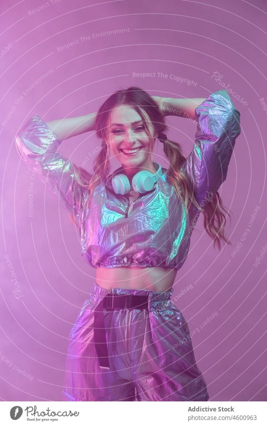 Futuristic female in stylish outfit standing in studio with neon illumination woman illuminate style smile futuristic headphones 80s personality happy portrait