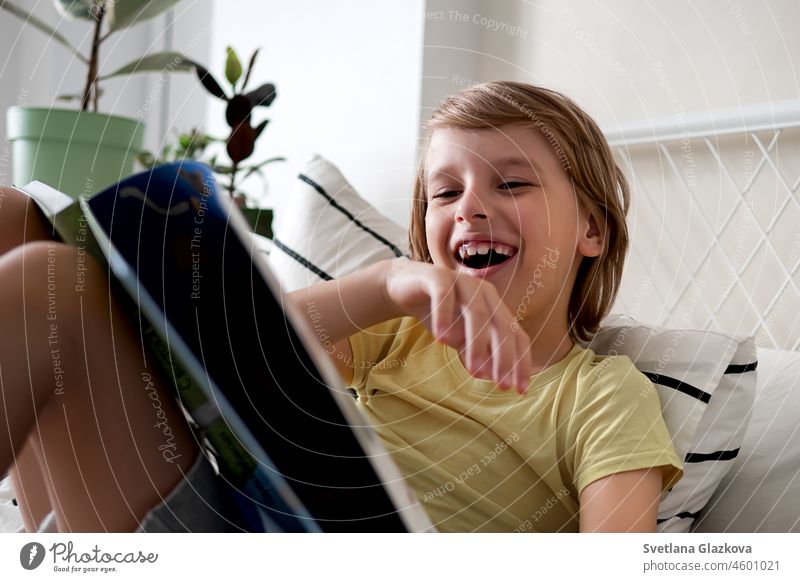 A blond boy in a yellow T-shirt reads a book while lying on the bed kid story childhood male son person caucasian ethnicity young youth youthful elementary