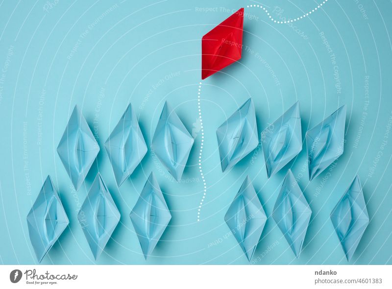 a group of blue paper boats heading in one direction and one red one heading in the opposite direction. The concept of individuality, uniqueness and talent of the employee. Get away from the influence