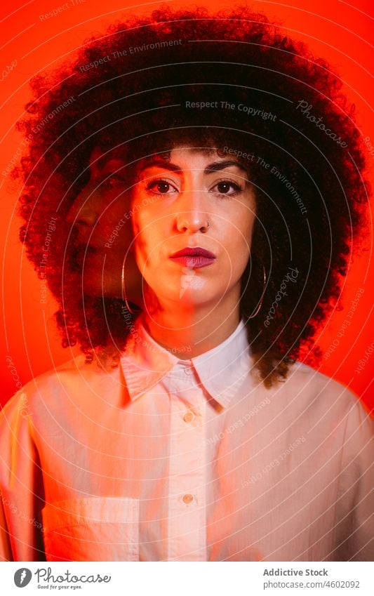 Serious Hispanic lady standing in studio with neon red lights woman serious model portrait appearance style confident self assured gorgeous emotionless fashion