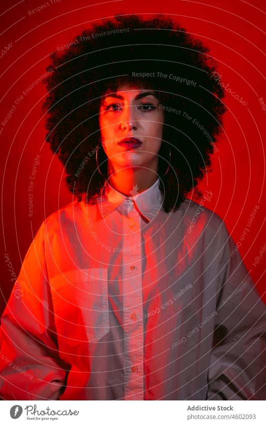 Serious Hispanic lady standing in studio with neon red lights woman serious model portrait appearance style confident self assured gorgeous emotionless fashion