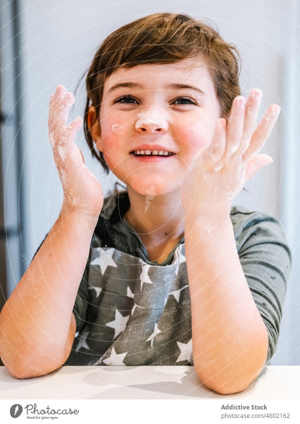 Positive girl with flour on face and hands kitchen cook culinary kid home domestic child helper apron pastry bake light smile homemade counter messy childhood