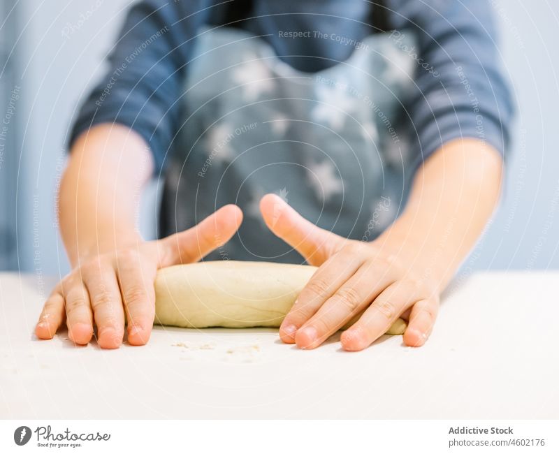 Anonymous boy kneading dough in kitchen cook kid flour pastry helper tear apron process bake food domestic child kitchenware culinary product messy dirty