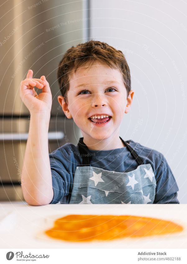 Smiling boy in apron in kitchen cook home kid domestic prepare child kitchenware culinary brown hair blue eyes at home charming cute innocent gaze helper