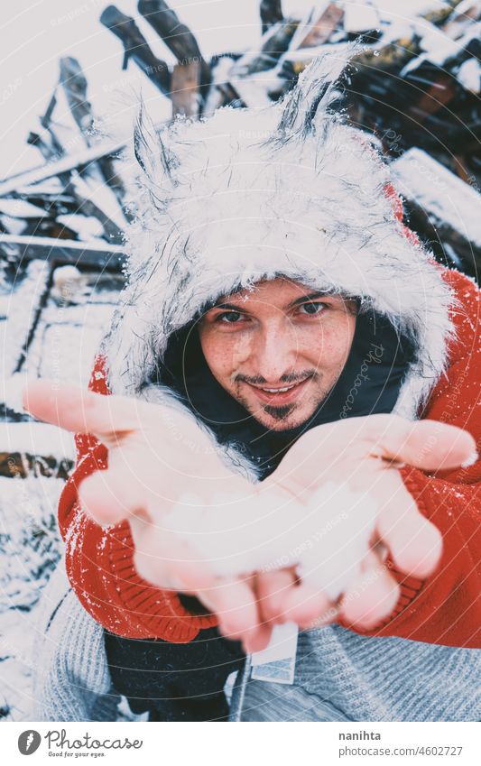 Young man enjoying a snowy day wearing a fur hat and a red hoodie winter fun funny cold freeze frozen life lifestyle white caucasian beard attractive cool fresh