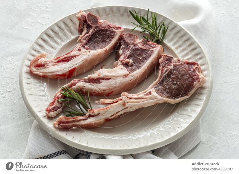 Raw lamb chops on plate raw meat serve rosemary uncooked food herb culinary table fresh delicious tasty ceramic kitchen cuisine ingredient light palatable