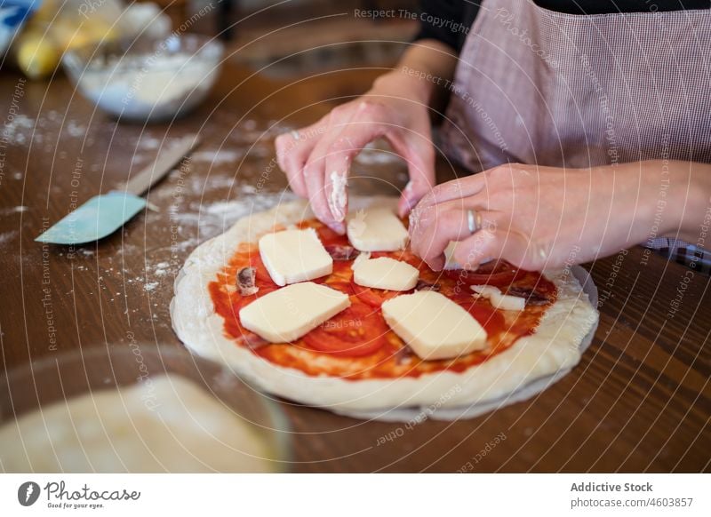 Faceless woman putting cheese on raw pizza cook dough mozzarella kitchen culinary homemade household cuisine prepare chef table apron process female light sauce