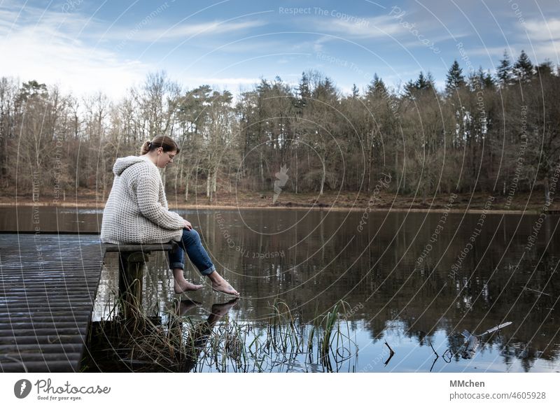 Woman sitting on jetty, stretching foot into water Lake crater lake Footbridge Feet Barefoot Water Surface of water Blue Cold reflection Nature Forest Landscape