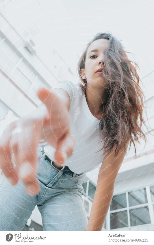 Young african arab poc woman posing trendy fashion to camera next to a group of buildings block with copy space. Cool and hip hop concept. Street style. Jeans and white shirt