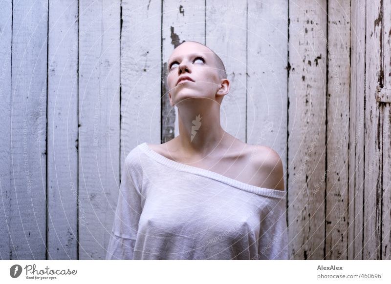 Young woman with a thin T-shirt in front of a board wall looks up into the light from the roof Youth (Young adults) Head Nipple Shoulder Freckles 18 - 30 years