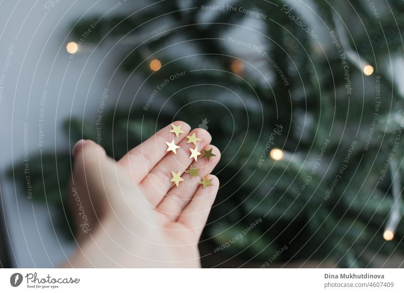 Hand holding glitter gold stars with christmas tree as background. Minimalist christmas photo. magical imagination illuminated creativity fairy fantasy