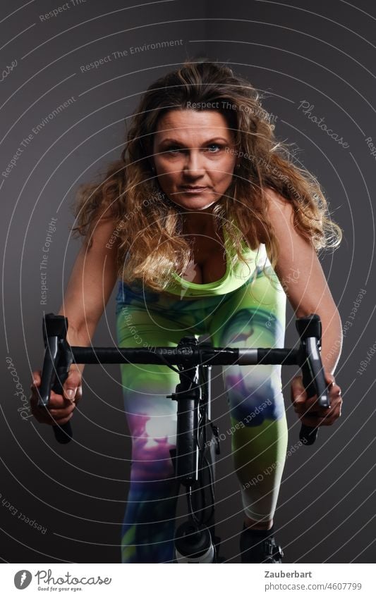 Sporty beautiful woman training on indoor racing bike Woman Athletic pretty exercise Racing cycle good resolutions Exercise bike Sports handlebars Green neon