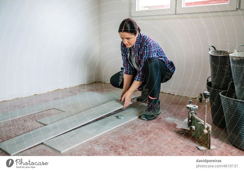 Female bricklayer placing tiles to install a floor female tiler woman crouched construction home worker repairing mason house manual worker laying build hand