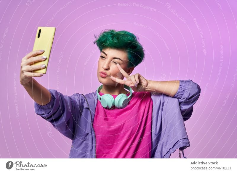 Cheerful millennial woman taking selfie smartphone self portrait social media headphones meloman style 80s fashion design retro studio green hair female model