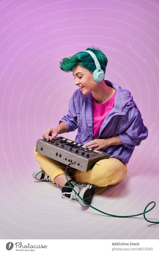 Positive millennial woman in headphones playing on keyboard controller compose 80s music musician style fashion design retro song audio studio green hair female