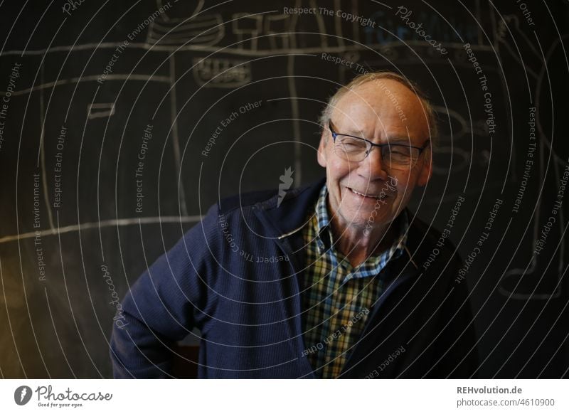 Senior laughs in front of black wall Front view Upper body portrait Male senior Man Grandfather Human being Head 60 years and older Gray-haired Eyeglasses