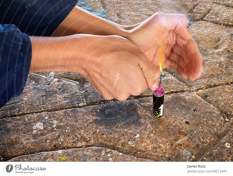 hands of a naughty child with a lighter lighting a large firecracker on the ground, sparks flying from the wick of the explosive about to go off and explode