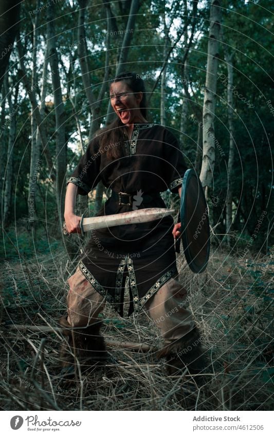 Angry female viking with weapon and shield during battle reconstruction woman attack dagger aggressive scream reenactment historic medieval conflict rage shout