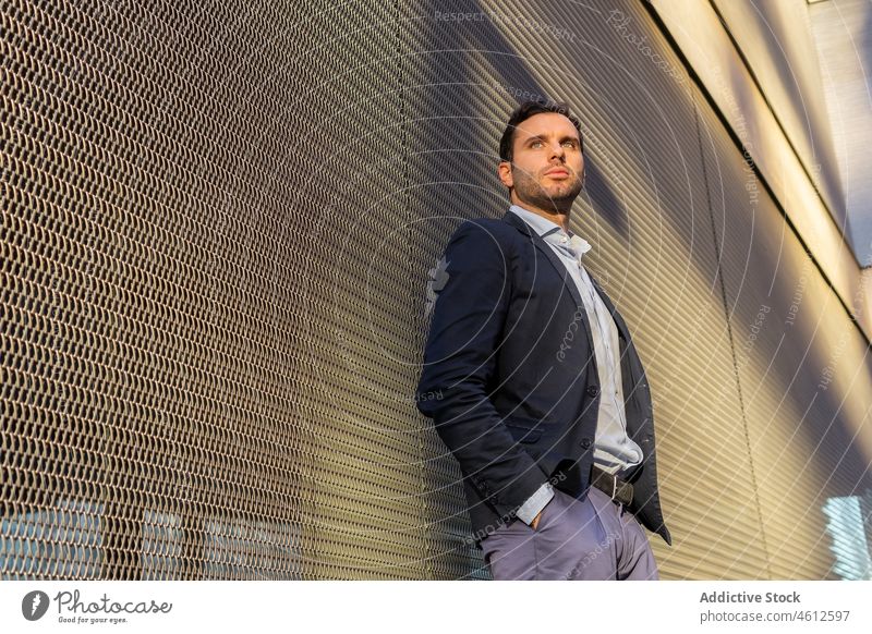 Serious businessman near wall on sunny street entrepreneur formal city urban sunshine shadow thoughtful male elegant appearance brunet beard suit well dressed