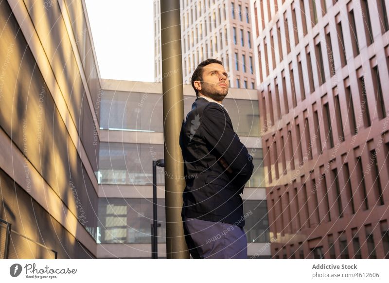 Positive businessman leaning on pole entrepreneur formal street city modern urban fence building male elegant appearance think brunet beard suit arms crossed