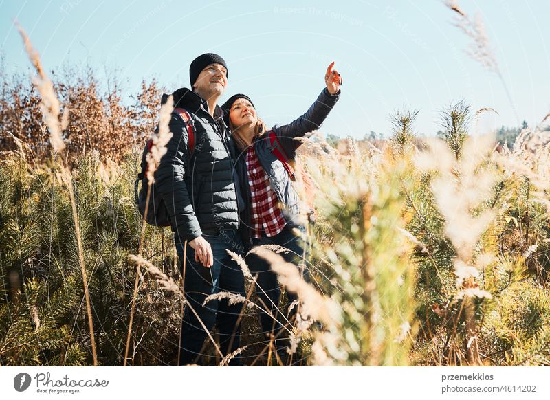 Couple exploring nature while vacation trip. Hikers with backpacks on way to mountains. People walking through tall grass along path in meadow on sunny day