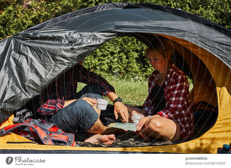 Couple planning next trip while sitting with map in tent. People relaxing in tent at camping during summer vacation adventure campsite traveling active