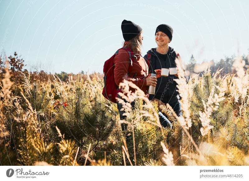 Friends relaxing and enjoying the coffee during vacation trip. People standing on trail drinking coffee. Couple with backpacks hiking through tall grass along path in mountains