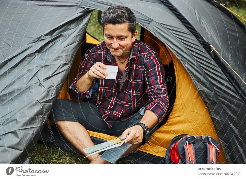 Man relaxing in tent at camping during summer vacation. Man holding map while planning next trip adventure campsite traveling active recreation equipment