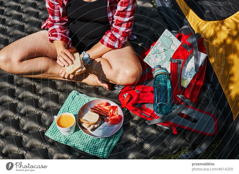 Woman having breakfast sitting by tent at camping. Female actively spending summer vacations close to nature outdoors trip adventure campsite traveling food