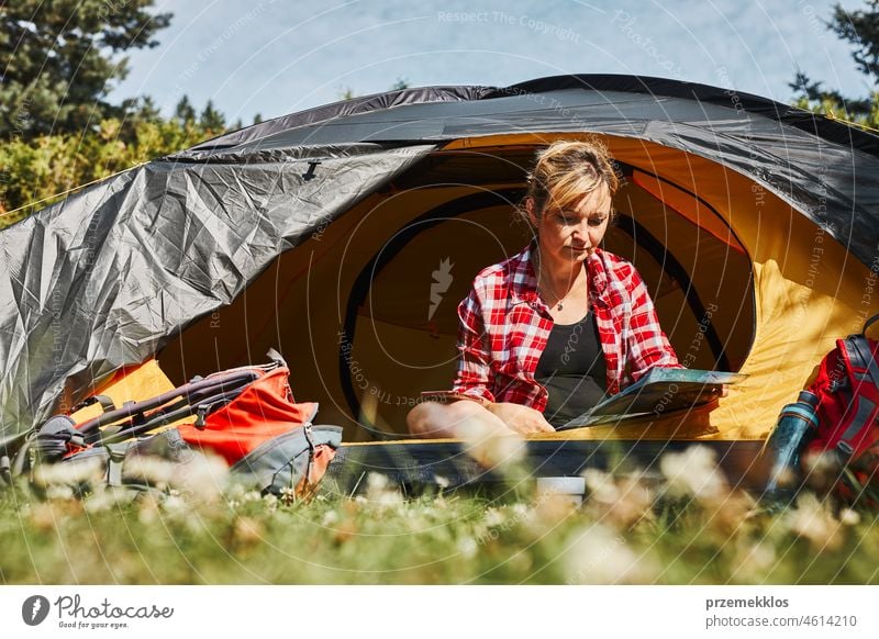 Woman planning next trip while sitting with map in tent. Woman relaxing in tent at camping during summer vacation adventure campsite traveling active recreation