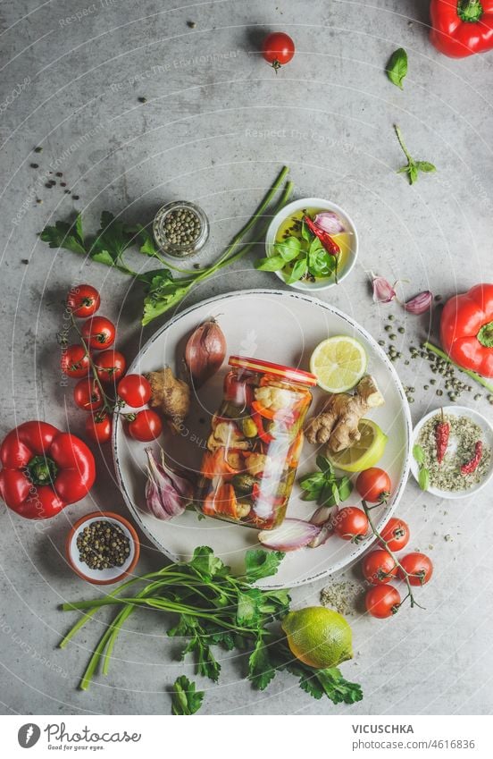 Preserved pickled vegetables in glass jar on white plate with herbs, vegetables and spices preserved grey concrete kitchen background fermenting healthy food