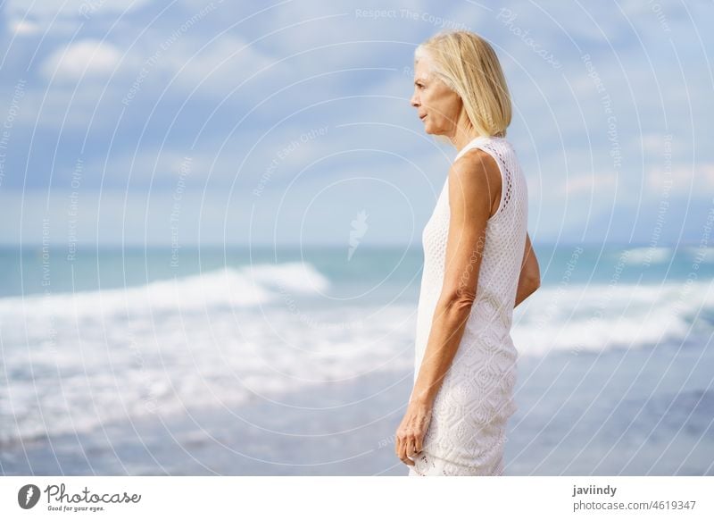 Mature woman gazing serenely at the sea. Elderly female standing at a seaside location mature senior beach smiling smile old caucasian person elderly retirement