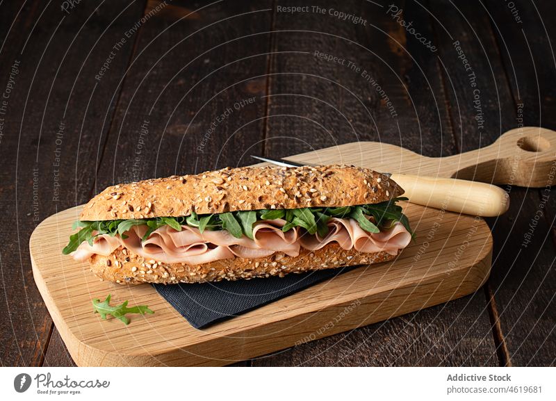 Ham sandwich with rocket leaves on wooden cutting board mediterranean mortadella baguette french bread meal food delicious rustic paper napkin panini snack ham