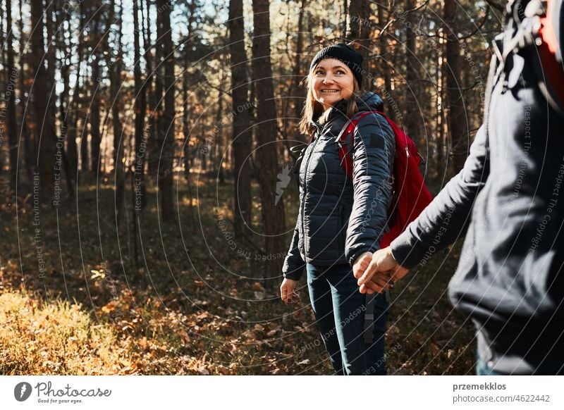 Couple holding hands enjoying trip while vacation day. Hikers with backpacks walking on forest path on sunny day hiking adventure travel gesture exploring